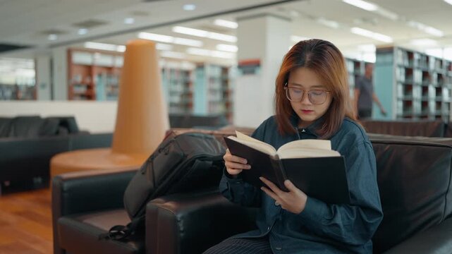 Asian university student wearing glasses reading books in a university library during intensive study or while working on a thesis or dissertation