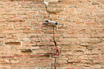 Electric digital crack measuring device reading, by cable, the minimal deformation and movement of a dangerous cracked brick wall
