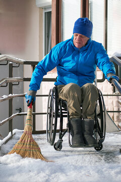 A wheelchair user in a blue jacket sweeps his ramp with a broom