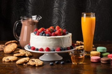 Deliciously decorated cake with fresh berries, cookies, macarons, and drinks