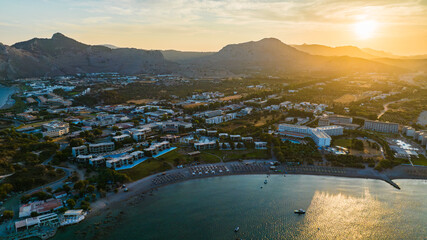 Aerial view of golden sunlight kissing the tranquil bay and sandy beach, contrasting with the rugged mountains, Rhodes, Greece.