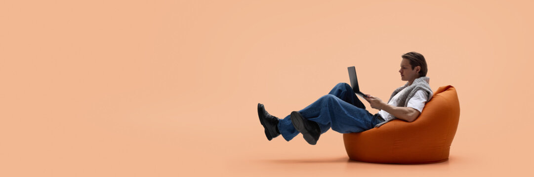 Man working on laptop while levitating on bean bag chair. Concept of startup culture, creative freelance work, content production, flexible workspace and long focused work cycles. Banner