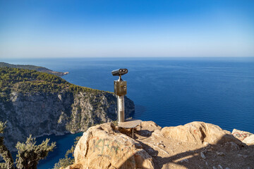 High angle view of a public binocular station on a rocky cliff overlooking the turquoise Butterfly Valley bay. Scenic panoramic vista of the Mediterranean coast near Oludeniz. September, Turkey