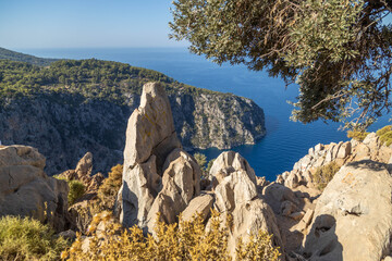 Breathtaking high angle view of jagged limestone cliffs and turquoise sea water. Scenic Mediterranean landscape in Faralya with wild vegetation and deep blue horizon. September, Turkey.
