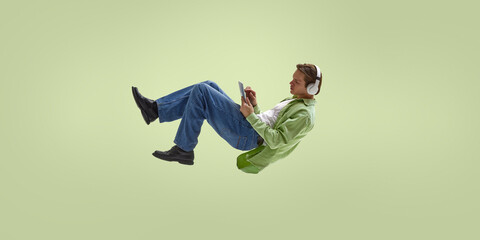 Young man using tablet with headphones while levitating in casual work posture. Concept of focused remote work, learning platforms, SaaS ecosystems, freelance routines and digital concentration.
