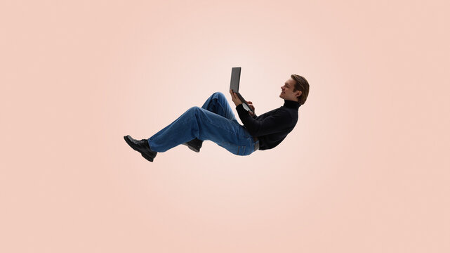 Casual man levitating with laptop on warm pastel background. Concept of relaxed workflow, reduced stress, intuitive technology use, comfortable remote routine and contemporary office culture.