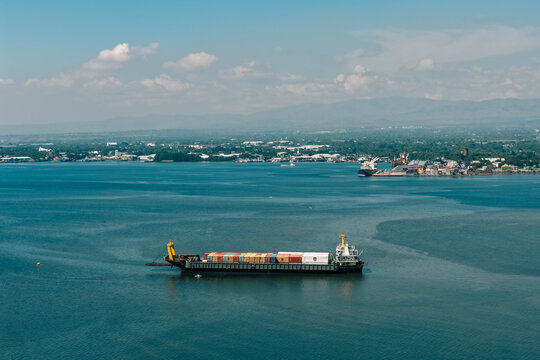 Aerial view of a cargo ship cuts across the still, turquoise waters, juxtaposed against the distant cityscape and verdant hills, General Santos, SOCCSKSARGEN, Philippines.