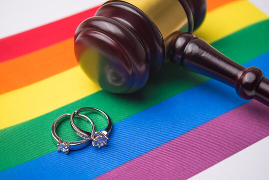 Close up wedding rings and judge wood gavel hammer on LGBT pride flag background with copy space. Legal status of same-sex marriage, LGBT human rights, equality and freedom concept. - Powered by Adobe