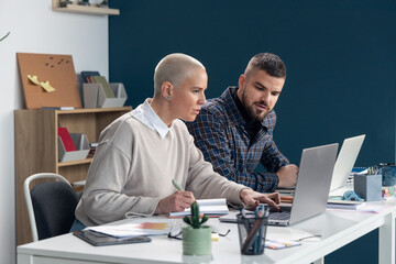 Coworkers collaborating on laptops at office desk