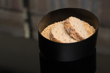 Artisanal sourdough slices elegantly presented in a modern black box on a bed of raw grains. Minimalist fine dining bread service, perfect for high-end restaurant menus and luxury food marketing.