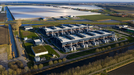 Aerial view of a vast data center's metallic structures gleaming against the soft, green fields and waterways, Data Center Agriport, Middenmeer, Netherlands.