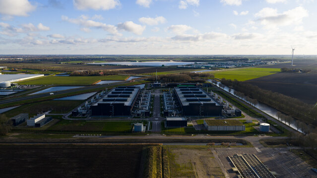 Aerial view of stark, dark buildings contrast against the bright green fields and blue sky, a modern industrial landscape, Data Center Agriport, Middenmeer, Netherlands.