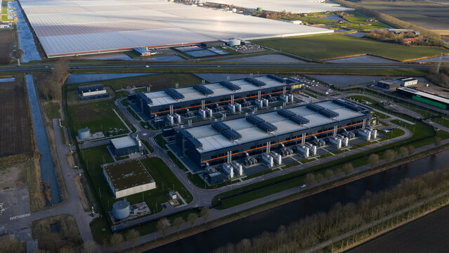 Aerial view of a sprawling data center complex with its geometric buildings contrasting against surrounding greenhouses, Agriport, Middenmeer, Netherlands.