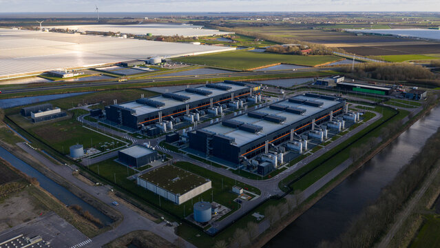 Aerial view of the Agriport data center complex reflecting the sun's rays, with greenhouses in the background, Middenmeer, Netherlands.