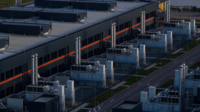 Aerial view of a modern, sprawling industrial complex with dark gray walls and light gray machinery stretching along a paved road, Data Center Agriport, Middenmeer, Netherlands.