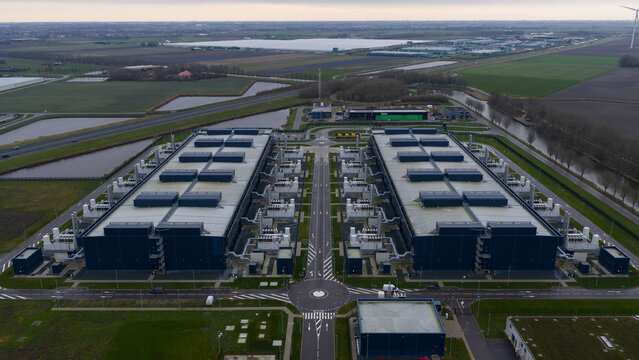 Aerial view of the vast data center complex with its dark roofs contrasting against the surrounding green fields, Agriport, Middenmeer, Netherlands.