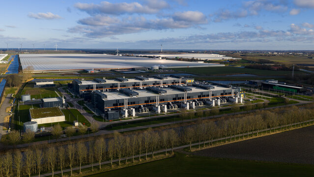 Aerial view of the expansive data center complex with its dark rectangular blocks contrasting with the surrounding bright greenhouses, Middenmeer, Netherlands.