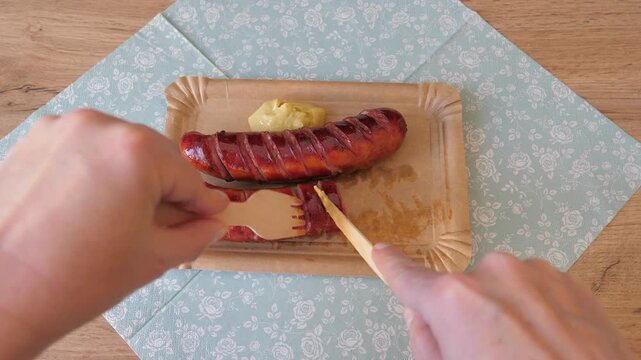 Eating grilled sausages with mustard on a paper picnic plate. Picnic food.
