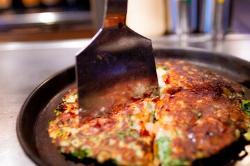 鉄板で焼いたお好み焼きをコテで切る