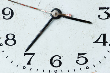 Close-up of old analog clock dial with distressed texture, black numerals, and visible hands.