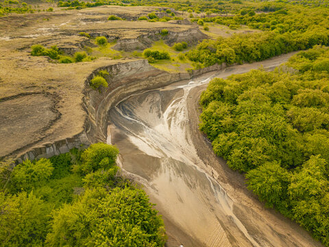 Aerial view of a river carving through arid terrain, bordered by verdant trees in a striking contrast of textures and tones, Huila, Huila, Colombia.