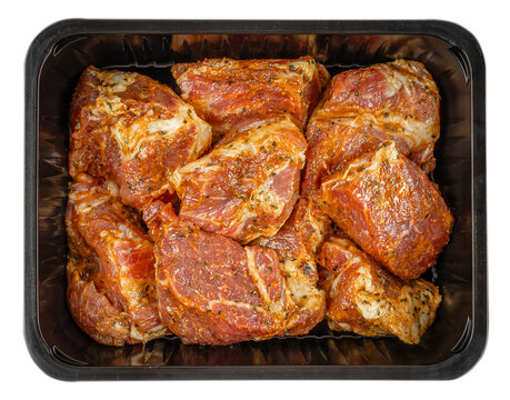 Top view of raw pork neck pieces coated in spicy herb marinade packed in black plastic tray, fresh meat preparation for roasting or grilling isolated 