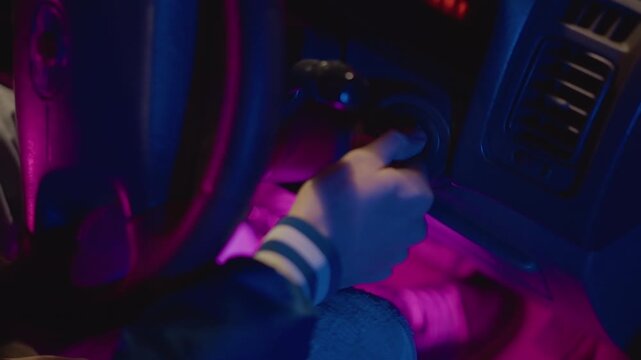 neonlit car interior hand turning key, pink and purple underglow, closeup wrist and dashboard lights, student driver fumbling for ignition, cinematic anticipation before latenight departure, grainy