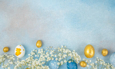 Elegant Easter flat lay with blue and gold eggs, white flowers and wide copy space on textured background