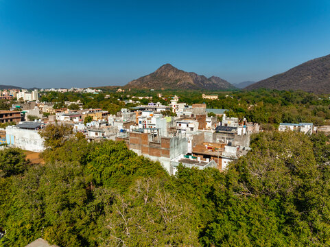 Aerial view of the town nestled among verdant trees, with the majestic mountains in the backdrop, Pushkar Rural, Rajasthan, India.