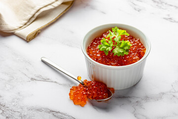 Red caviar bowl and spoon on marble with beige napkin