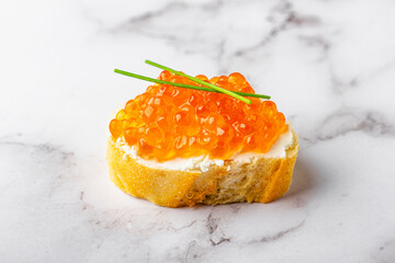 Slice of baguette with red caviar and cream cheese on marble surface