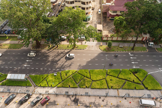 High-angle aerial view of a clean city street with cars, motorcycles, lush green landscaping, and modern urban architecture