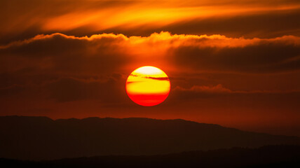 Vibrant orange sunset over mountain range with dramatic clouds