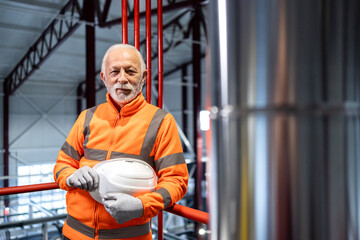 Senior male worker holding hardhat in refinery