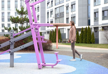 Young woman exercising on outdoor fitness equipment in an urban residential area. Active lifestyle