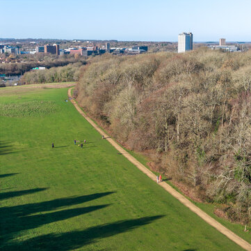 Aerial view of a vibrant green park contrasting with the stark trees and distant buildings, a pathway inviting exploration, Basingstoke, England, United Kingdom.