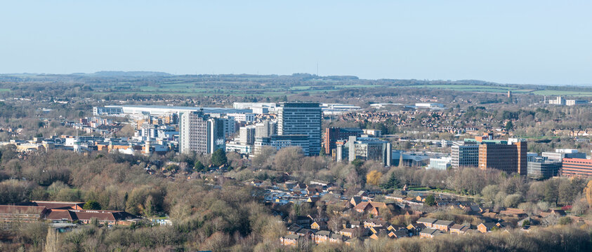 Aerial view of a cityscape with tall buildings rising above a dense forest, contrasting with the clear blue sky, Basingstoke, England, United Kingdom.