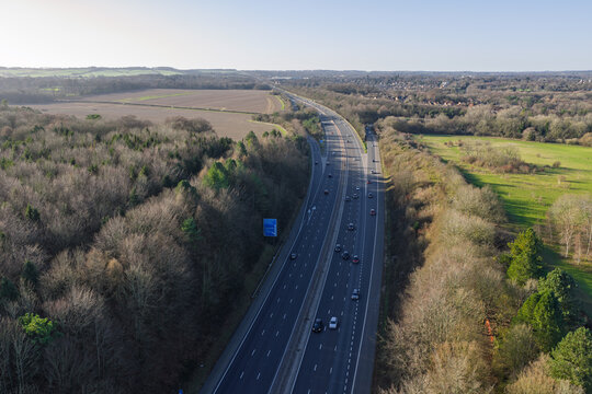 Aerial view of the M3 motorway cutting through fields and woodland, a ribbon of grey amid the greens and browns, Basingstoke, England, United Kingdom.