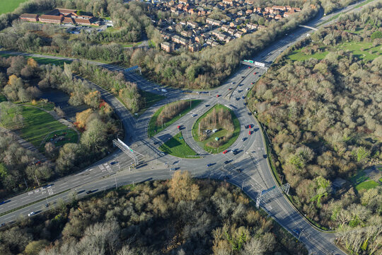 Aerial view of a bustling roundabout intertwines with roads amid the lush greenery and autumnal hues near Basingstoke, England, United Kingdom.