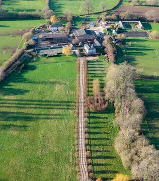 Aerial view of a quaint farmstead nestles amidst verdant fields, bisected by a tree-lined path casting long shadows, Hartley Wintney, England, United Kingdom.