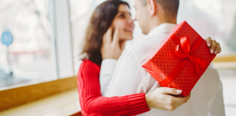 Man gives to his woman a gift box with red ribbon. A loving couple celebrating Valentine's Day.