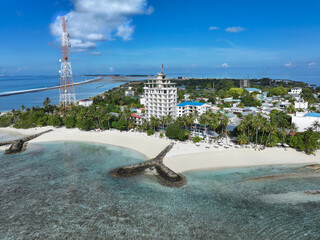 Aerial view of the island's white sandy beach meeting the turquoise waters, overlooked by a tall building and a telecommunication tower, Thulusdhoo, Kaafu Atoll, Maldives.