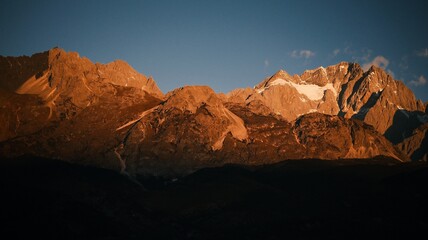 Sunrise Glow on Jade Dragon Snow Mountain over Lijiang Old Town, Yunnan, China.