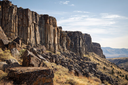 Rugged rocky cliff formation stretching across dry hilly landscape under a clear sky with distant mountain ranges on a sunny day
