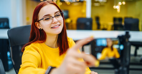 Female blogger with laptop recording video while sitting at office and talking about startup...