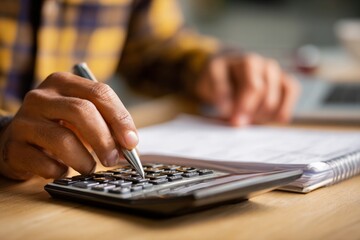 Hand using calculator for monthly budget planning financial document pen and notebook on wooden desk close up home office focused personal finance and spending review