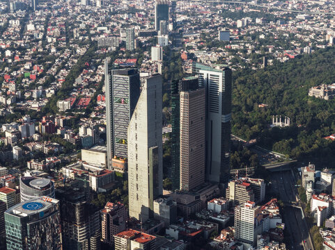 Aerial view of towering skyscrapers piercing the sky along Paseo de la Reforma, where glass facades reflect the sun amidst the lush greenery, Mexico City, Mexico City, Mexico.