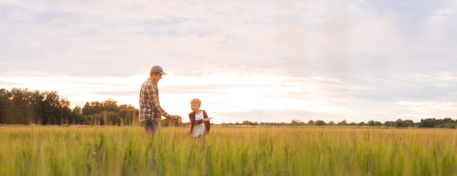 Farmer and his son in front of a sunset agricultural landscape. Man and a boy in a countryside field. Fatherhood, country life, farming and country lifestyle concept.