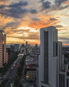 Aerial view of the Monument to the Revolution stands silhouetted against a fiery sunset, its stark white facade contrasting with the warm hues of the sky, Mexico City, Mexico.