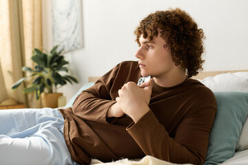 Curly teenager relaxing in his modern bedroom surrounded by cozy decor